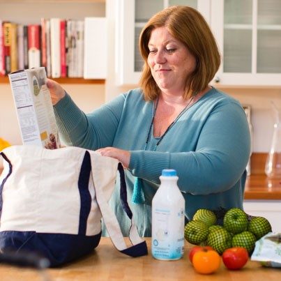 Woman unpacks groceries in kitchen.