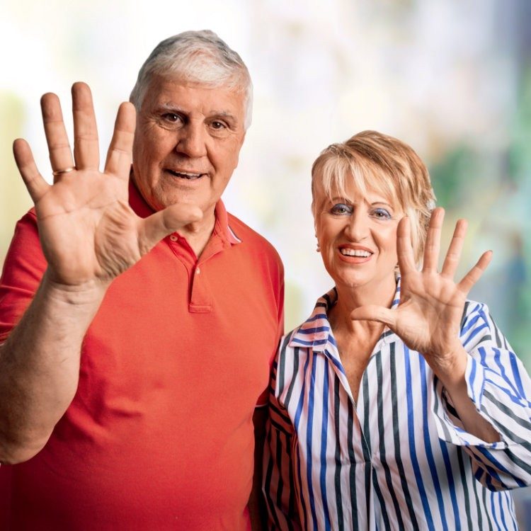 Elderly couple standing together and making a high five gesture towards the camera