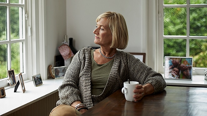 Adult female in gray sweater sitting at a table with a coffee mug and looking out the window