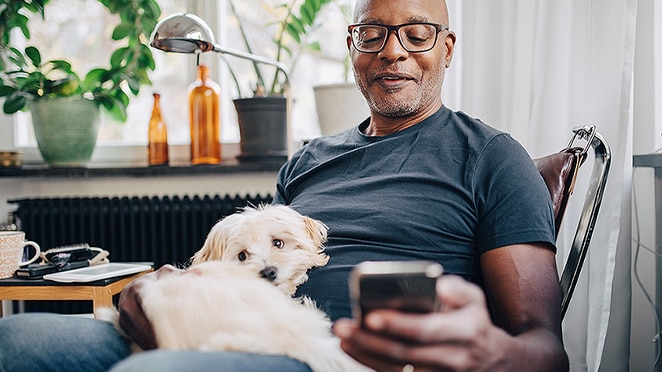 Man sitting with dog on his lap and looking down at his smartphone