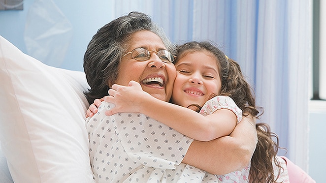 Older female in a hospital gown embracing a young girl while lying in a hospital bed