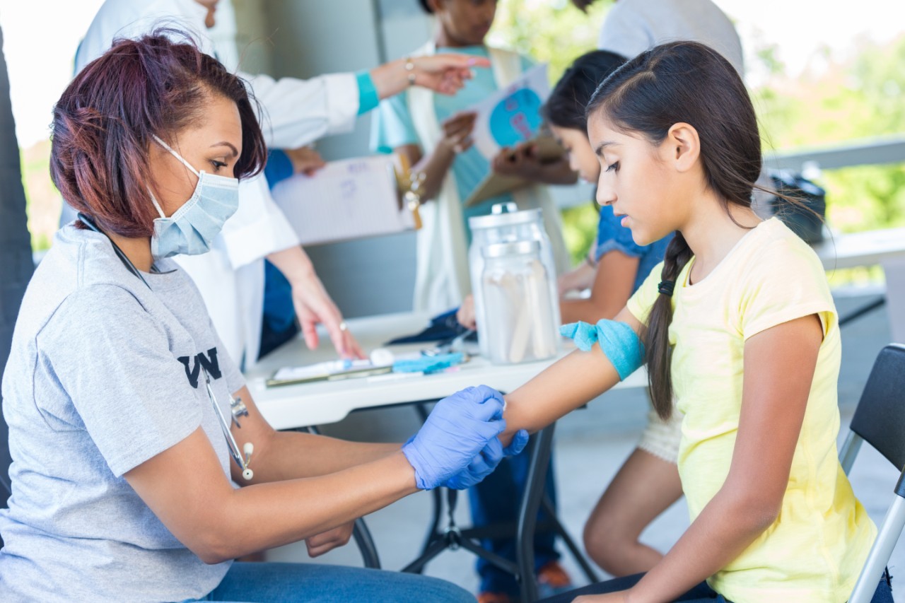 A medical professional draws child's blood outside