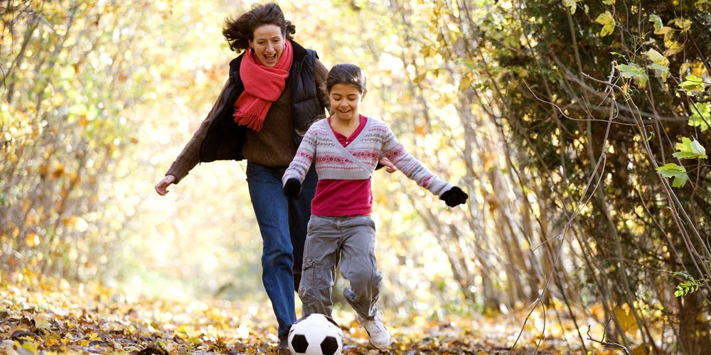 A mother and her daughter with soccer ball in the woods.