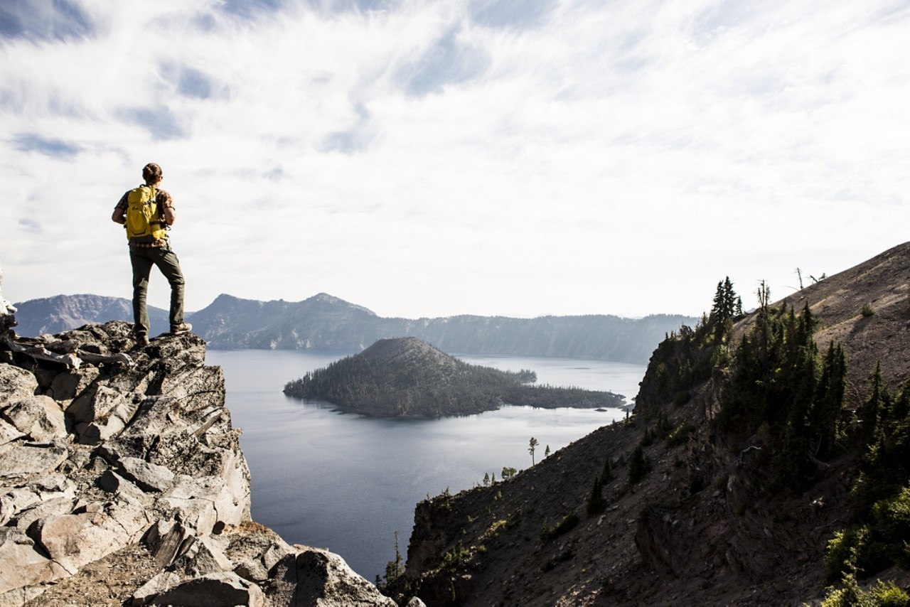 Person standing on top of mountain looking at lake below