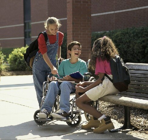 Two children talk and laugh with their friend that is in a wheelchair, happy and enjoying life.