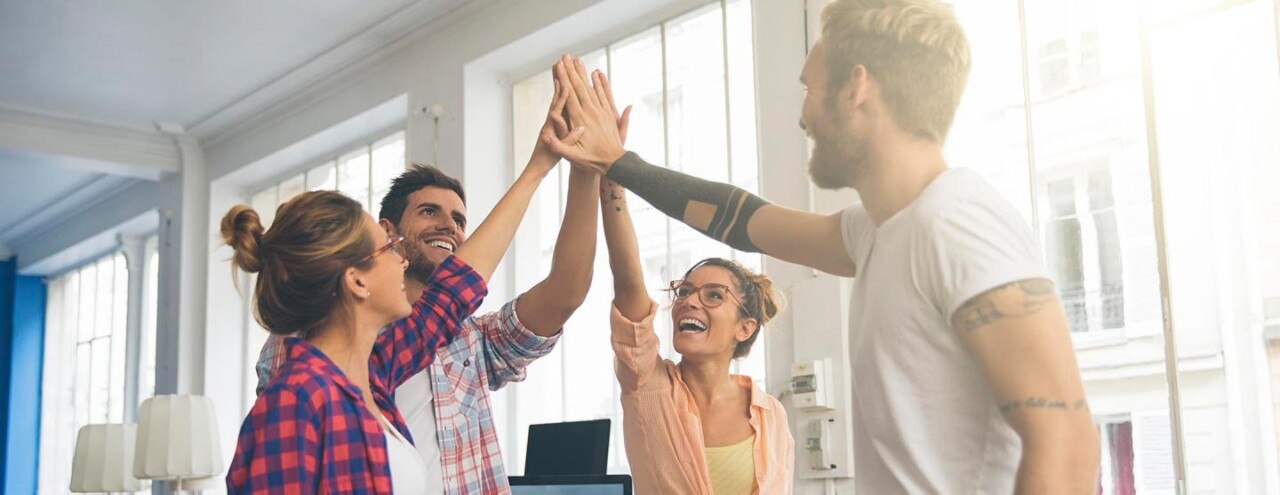 Four people in bright office celebrating with high-five, thumbnail image crop