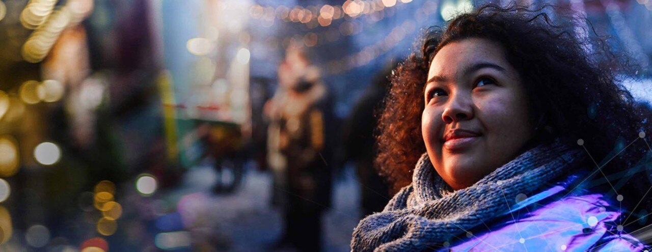 Woman outdoors at a winter fair in a city with lights and buildings in the background.