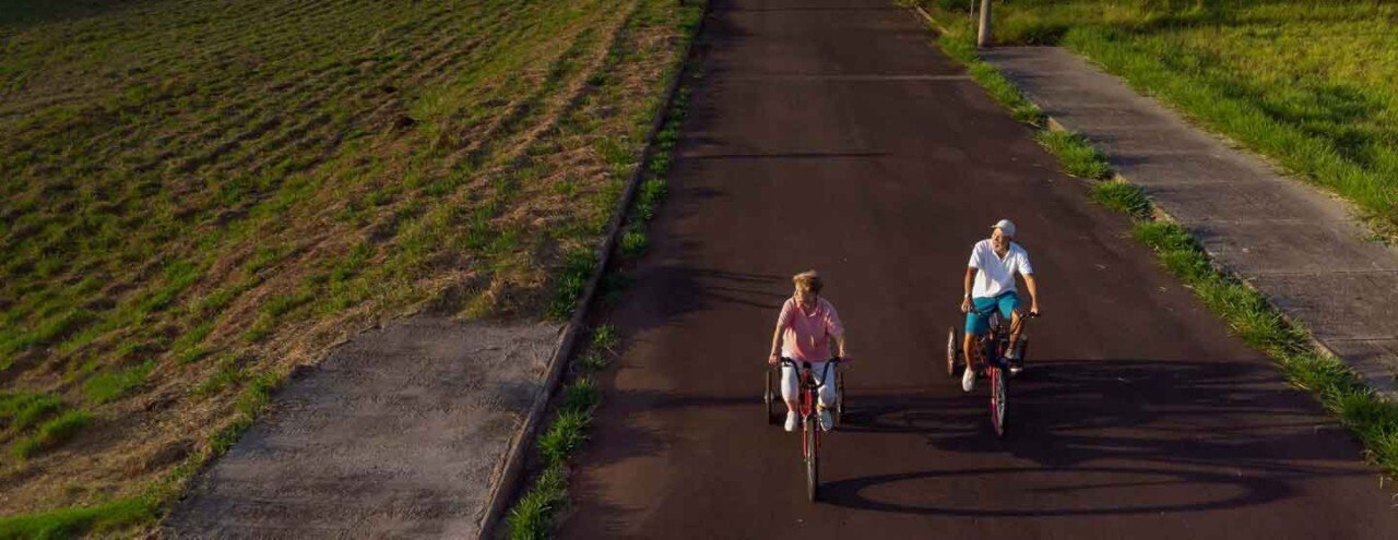 A woman and a man riding their bicycles on a country road near farmland