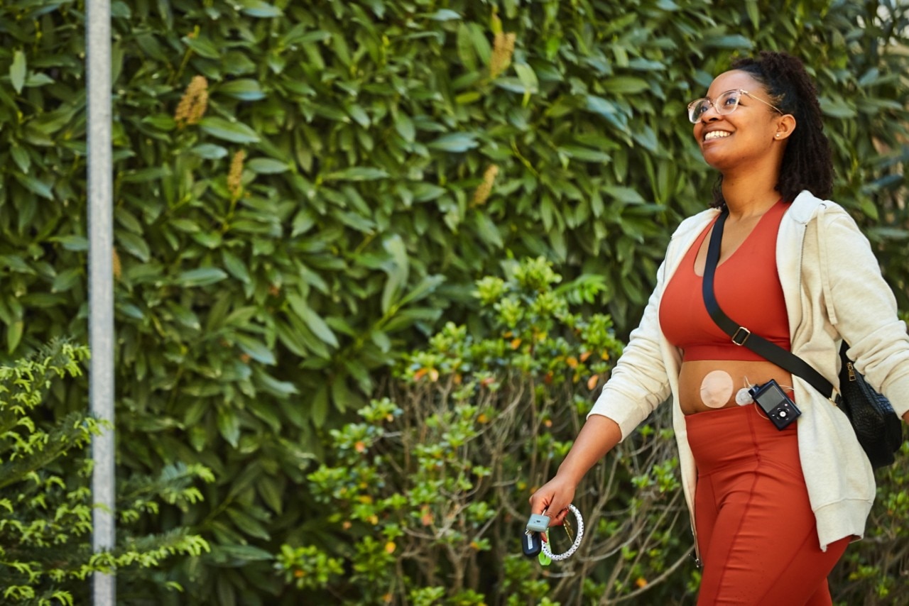 A woman is walking in a park wearing a medical device with a monitor attached  to her waist.