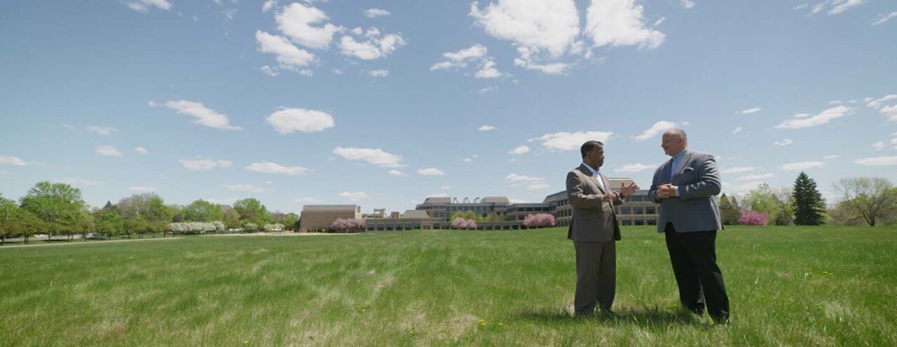 Two men standing  and talking in open field front of Medtronic headquarters building.
