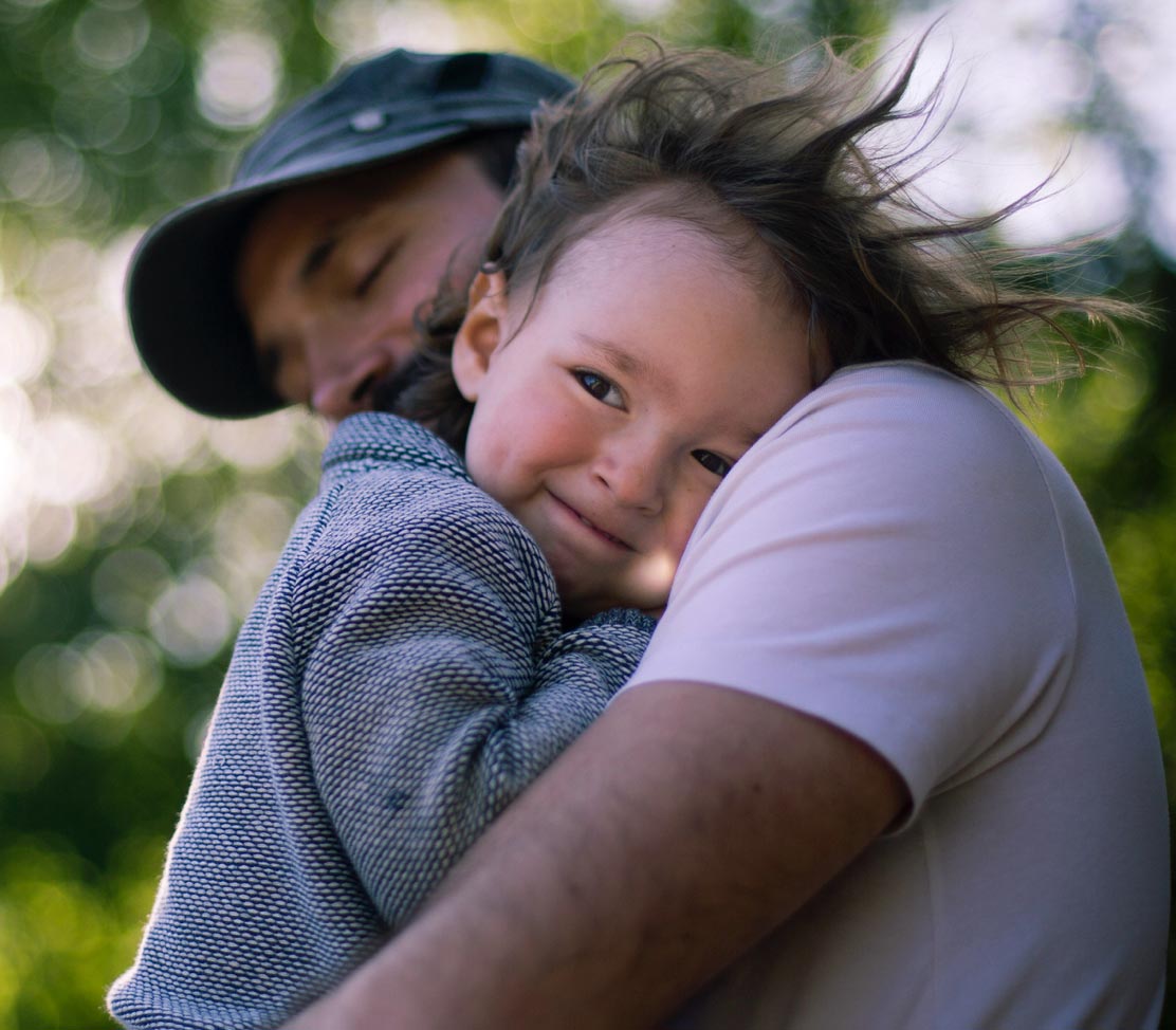 Man hugging child outdoors with trees in background