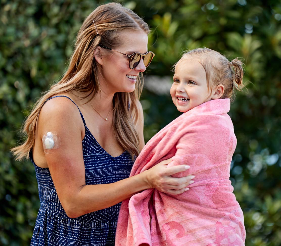 Mother and daughter outdoors in swimming towel with diabetes product Guardian Connect